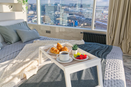 White Tray with tasty breakfast on bed in light bedroom with big windows in skyscraper. lifestyle