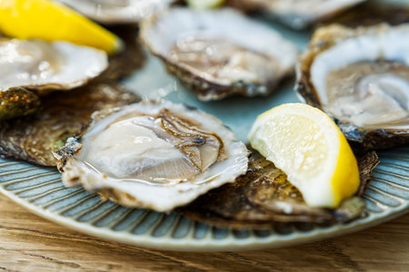 Fresh oysters served on a plate with lemon on old wooden table. Oysters served in fish restaurantの写真素材