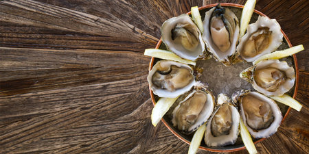 Fresh oysters served on a plate with lemon on old wooden table. Oysters served in fish restaurantの写真素材