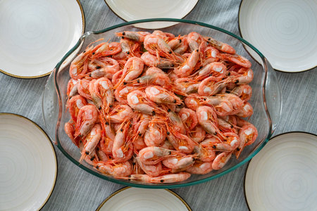 A dish of unpeeled shrimp on a dinner table with plates. Seafood diner. Boiled shrimps.の写真素材