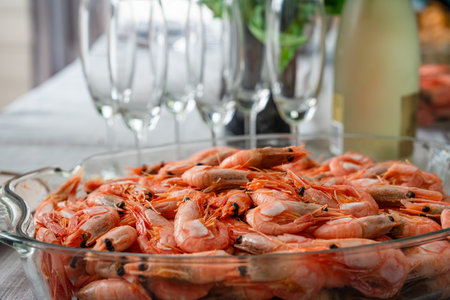 A dish of unpeeled shrimp on a dinner table with plates. Seafood diner. Boiled shrimps.の写真素材