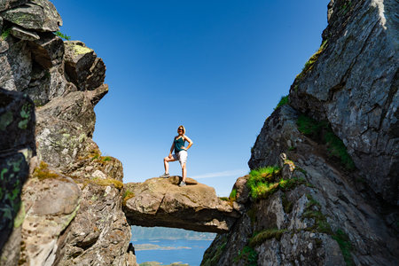 Brave traveler woman standing on hanging stone between rocks. Djevelporten in Norway Lofoten islandsの写真素材
