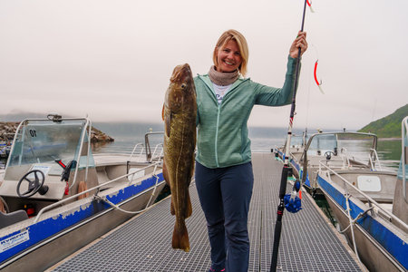 Happy Fisherwoman holding big arctic cod. Norway happy fishing. Woman with cod fish in hands
