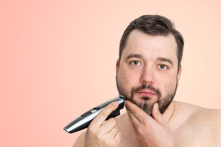 unshaven young man perfect skin hold electric razor shaving, isolated. Grooming for the modern manの写真素材