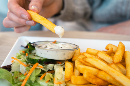 Woman hand dipping delicious French fries into mayonnaise sauce, cheese sauce.の写真素材