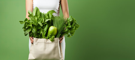 Eco friendly person holding reusable tote bag with local vegetables on green backgroundの素材