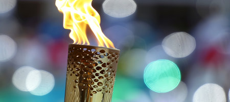 Olympic torch flame burning against blurred sports arena with copy space for textの素材