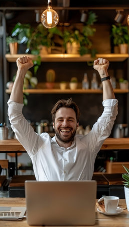 Excited young businessman triumphantly celebrating success in front of open laptopの素材
