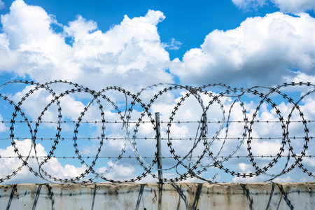 Barbed wire securing the top of a concrete fence wall for enhanced security measuresの素材