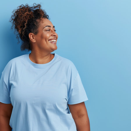 Confident overweight woman in blue shirt smiling, curly hair, pastel blue backgroundの素材