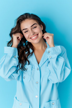 Confident curly haired plus size woman in blue shirt smiling against soft blue backgroundの素材