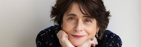 Portrait of a Confident and Smiling Senior Woman Resting Her Head in Her Hands Against a Gray Wallの素材