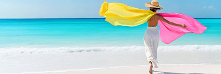Woman with flowing yellow and pink fabrics walks on a tropical beach, enjoying summer vacation.の素材