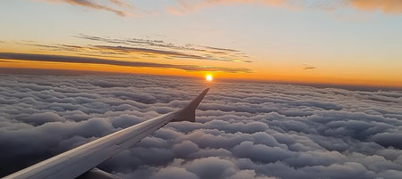 Scenic Sunset Over a Fluffy Cloudy Sky From Airplane Wing on Background. Plane Wing Silhouetteの素材