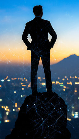Silhouetted Businessman Standing on a Mountain Peak, Overlooking a Glowing Cityscape at Sunsetの素材