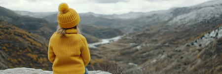 Young Girl in a Yellow Knit Hat and Sweater Contemplates the Beauty of a Winter Mountain Landscapeの素材
