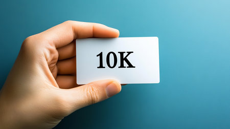Hand Holding White Card with the Text 10K Isolated on a Blue Background, Representing Achievement.の素材