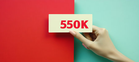 Female Hand Holding White Card With Text 550k On Colorful Split Blue And Red Background. Flat Lay.の素材