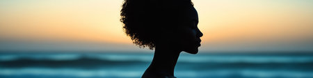 Silhouette Of A Black Woman Meditating By The Ocean Against A Beautiful Vibrant Sunsetの素材