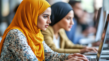 Focused Muslim Businesswomen in Hijab Working Diligently on Laptops, Office Collaborationの素材