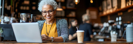 Smiling Female Owner Uses Laptop in Trendy Coffee Shop, Customers Blurred in Backgroundの素材
