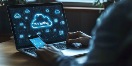 Businessman Using Mobile Device To Access Cloud-Based Marketing Automation Software On Laptopの素材
