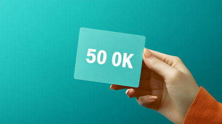 Woman s hand holding a green card with 50 OK text, isolated on a vibrant turquoise background.の素材