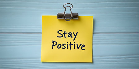 Yellow Sticky Note with Stay Positive Message, Attached with Metal Clip on Wooden Backgroundの素材