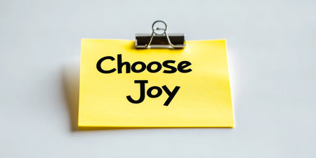 Yellow Sticky Note With Choose Joy Text Attached to The White Wall Using A Binder Clip.の素材