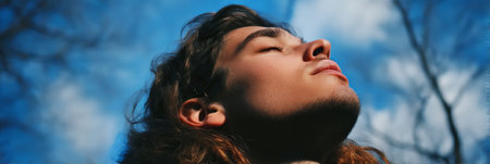 Young Man with Long Flowing Hair Soaking in Sun and Fresh Air with Eyes Closed, Nature Portrait.の素材