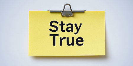Stay True Text on Yellow Sticky Note Attached with Metal Clip Against a Gray Backgroundの素材