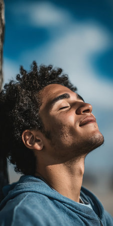 Young Man with Eyes Closed, Basking in Fresh Air and Sunlight Under a Vibrant Blue Skyの素材