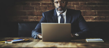 African American Senior Leader Working Casually on Laptop in Internet Cafe with Social Distancingの素材