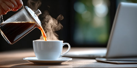 Steaming Coffee Pour to Cup on Desk with Laptop, Enjoying Daily Dose of Brew Amid Desk Landscape.の素材