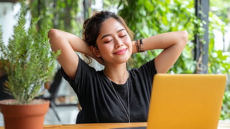 Content Asian lady finishing remote workday, stretching in a lush green office environment.の素材