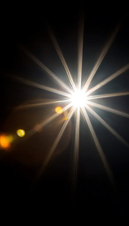 Starburst lens flare illuminating a dark canvas, creating a celestial and bright abstract feel.の素材