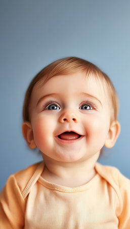 Adorable Little Baby on Soft Blue Background Looking Up with Pure Joyful Smile and Sweet Expressionsの素材