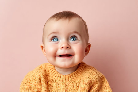Adorable baby portrait with blue eyes and joyful smile in an orange sweater on pink backdrop.の素材
