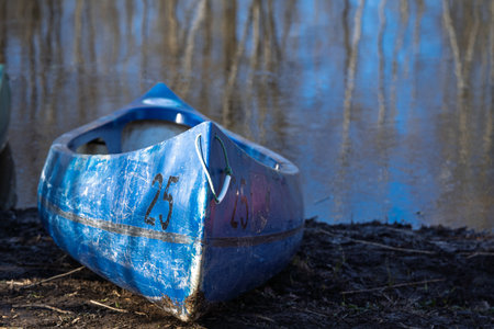 Weathered Blue Canoe on Muddy Shoreline with Water Reflection Backdrop, Ready for Adventureの写真素材