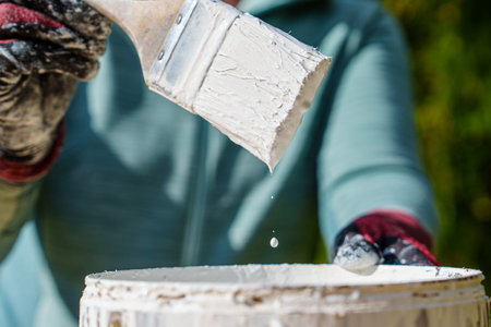 Close-up of Paintbrush Dripping White Paint into Can, Preparing for Home Improvement Projectの写真素材