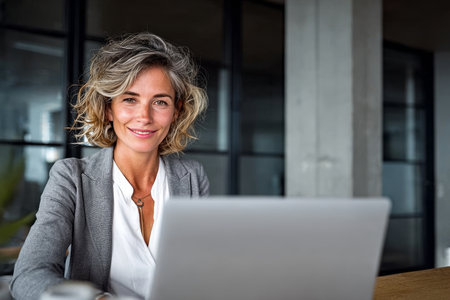 Focused CEO working on laptop in modern office space, exemplifying strong leadership skills.の素材
