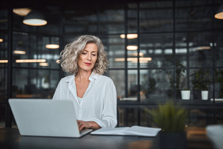 Professional Businesswoman in Elegant Dress Using Computer for Corporate Report in Modern Officeの素材