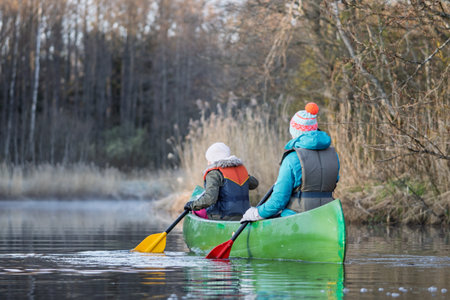 Family Adventure Paddling a Canoe on a Calm River, Surrounded by Autumnal Beautyの写真素材