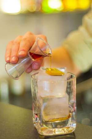 Hand pouring liquor on an ice cube in a glassの写真素材