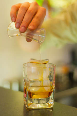 Hand pouring liquor on an ice cube in a glass