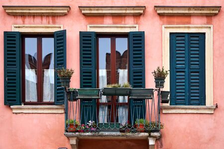 Ancient facade of the building. Balcony and two windows. Flowers on the balcony.の写真素材