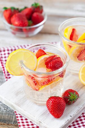 Refreshing homemade lemonade with fresh strawberry, lemon and ice. Healthy cold drink, low calories. Tasty cool summer beverage. Wooden white background, two glasses. Macro, close upの写真素材