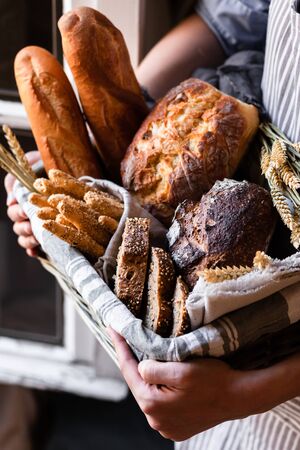 Concept of homemade bread, small bakery, natural farm products, domestic production. Healthy and tasty organic food. Woman holding basket with various bread freshly baked. Close upの写真素材