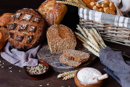 Concept of homemade bread, natural farm products, domestic production. Healthy and tasty organic food. Cut bread, milk, flour. Wheat spica as decor. Closeup, dark wooden backgroundの写真素材