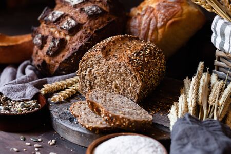 Concept of homemade bread, natural farm products, domestic production. Healthy and tasty organic food. Cut bread, milk, flour. Wheat spica as decor. Closeup, dark wooden backgroundの写真素材